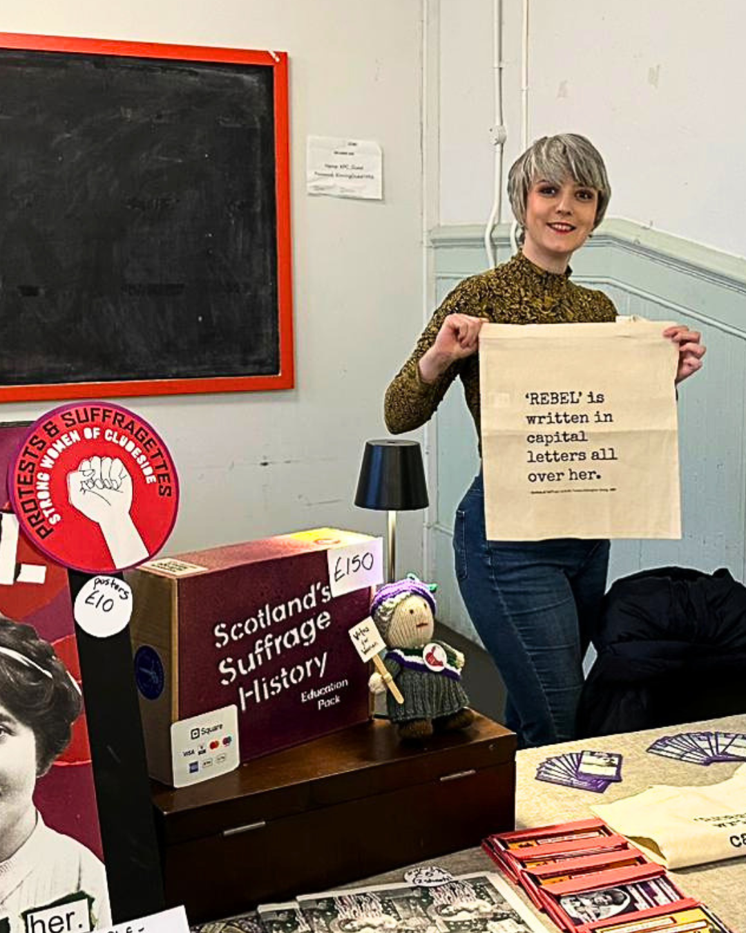 A Protests and Suffragettes volunteer holding a tote bag reading REBEL is written in capital letters all over her.